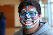 © NeedMoreMars - A teenage Hispanic boy with colorful face paint smiling brightly at an event, showcasing creativity and cultural expression in a vibrant indoor setting.