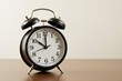 © NeedMoreMars - A Classic Vintage Black Alarm Clock Displayed on a Wooden Table against a Minimalistic Wall Background, Emphasizing Timeliness and Simplicity in Everyday Life