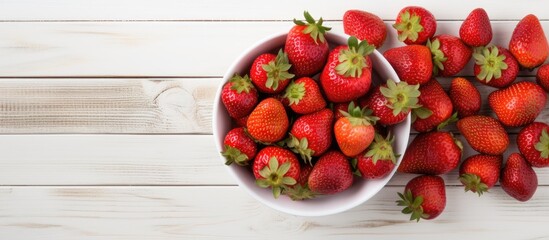 Poster - Fresh red strawberries in a white bowl placed centrally on a white wooden background with scattered strawberries creating a vibrant contrast.