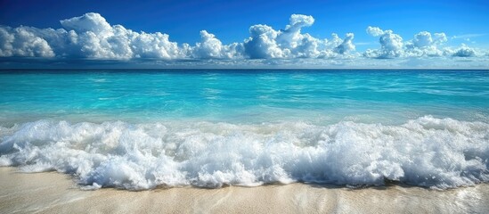 Aufkleber - Blue ocean waves crash onto a sandy beach under a bright blue sky with fluffy white clouds creating a serene tropical paradise atmosphere