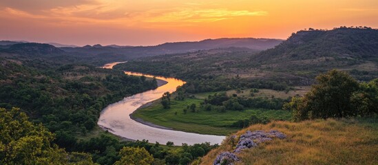 Poster - Warm twilight illuminates a winding river winding through a lush valley with gentle hills and a serene dusk sky filled with soft orange hues.