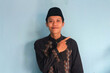 © Lailar Studio - Young Asian Muslim man wearing koko and peci smiling while pointing finger up