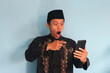 © Lailar Studio - Young asian muslim man looking at mobile phone screen with surprised expression