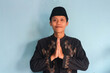 © Lailar Studio - Happy smiling young Asian muslim man standing with gesturing Eid Mubarak greeting and welcoming Ramadan