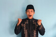© Lailar Studio - Excited young Asian Muslim man raising fists and celebrating victory on Ramadan and Eid Mubarak
