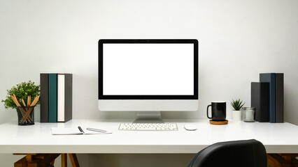Front view desktop computer with blank screen, books, coffee mug and decorative plants