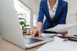 © wichayada - Businesswoman managing tax documents and finances at her desk with a laptop.
