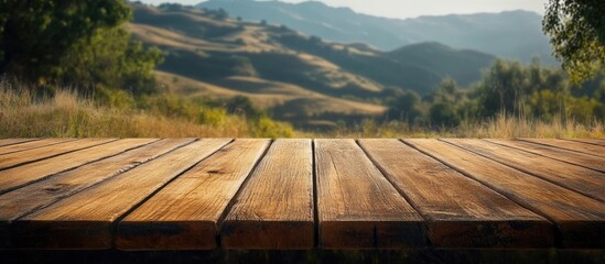 Leinwandbilder - Wooden deck table in the foreground with a rustic hillside and soft green hues in the background, showcasing a serene and inviting outdoor scene.