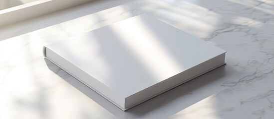 Poster - Minimalistic white book mockup positioned at an angle on a marble surface with soft natural light casting shadows highlighting its clean design.