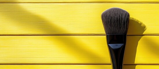 Leinwandbilder - Retro yellow wooden background with a makeup brush casting a strong shadow creating visual contrast and ample copy space on the left side.