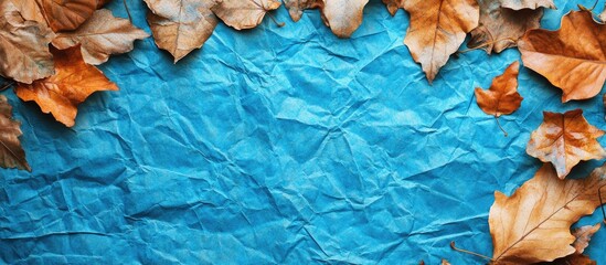 Aufkleber - Crumpled blue paper positioned centrally with dry orange and brown autumn leaves framing the top and sides creating a textured background with copy space