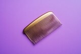 A single gold hair comb rests on a simple purple background