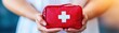 © Manita - A person holding a red first aid kit, emphasizing safety and preparedness for emergencies.