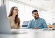 © Vadim Pastuh - A young woman and a man in a denim shirt are laughing while engaged in a friendly business conversation in a bright, modern office space