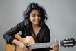© Markus Schröder - Portrait of a grinning indian woman in her 30s playing the guitar over soft gray background