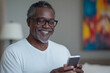 © Michael - Senior man smiling while using smartphone at home, enjoying mobile technology and staying connected in retirement
