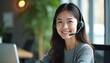 © miss irine - Smiling asian woman works on laptop at helpline support call center. Portrait of young business woman in headset looks at camera in office. Friendly receptionist gives support for customer service.