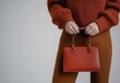 © Rock  - Photograph of a woman holding an elegant handbag with her hands, wearing brown pants and a sweater on a white background