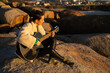 © asier - Female musician playing acoustic guitar on rocky shore, punta faxilda, silhouetted against golden sunset, capturing serene musical moment