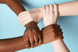 © New Africa - Stop racism. People of different skin colors joining hands on light blue background, closeup