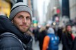 © Milos - A man wearing a knitted cap glances back over his shoulder in a busy city street, creating a portrait that captures the essence of modern urban life and movement.