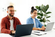 © Kateryna - A man and a woman are sitting at a desk working on their laptops, successful colleagues are smiling and looking at their screens, enjoying the productive atmosphere in the modern office