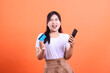 © Ajab - A young happy woman holding a credit card and device mobile phone, looking excited about online shopping, she has a bright smile, isolated on orange background