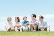 © buritora - 青空の見える公園・丘に座る家族・親子・三世代家族（父親・母親・娘・祖母・祖父）