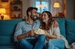 © miss irine - Couple laughs watching film on sofa at home. Man embraces woman, hold bowl with popcorn, enjoy movie night, relax in living room. Leisure time, home entertainment, relationships, happy together.