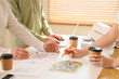 © Pixel-Shot - Team of constructors with coffee and house plan working at table in office, closeup