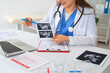 © Pixel-Shot - Female gynecologist with sonogram image at desk in office, closeup