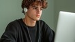 © NKTN - A young man with curly hair, wearing earphones, focuses intently on a computer screen in a calm setting