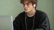 © NKTN - A young man with curly hair, wearing earphones, focuses intently on a computer screen in a calm setting