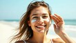 © ArtisticLens - Smiling young woman applying sunscreen on her face at sunny beach