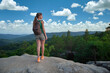 © bilanol - Active way of life concept. Young woman hiker standing alone on mountain footpath enjoying view of summer nature on wilderness trail