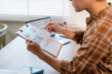 Poster - Businesswoman reviewing financial data, using pen and clipboard to analyze charts and graphs at her office desk