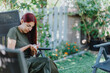 © qunica.com - A young woman sits peacefully in a garden, gently holding a small lizard. She is surrounded by vibrant greenery and outdoor seating.