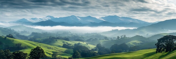 Aufkleber - Stunning green hills with snow capped mountains and misty peaks under an expansive sky filled with clouds