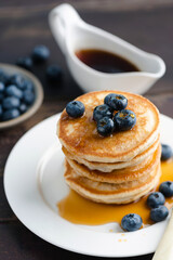 Wall Mural - Pancakes with blueberries stack on white ceramic plate served with maple syrup, closeup view