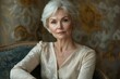 © Vibu design  gallery - Elegant older woman with short gray hair, wearing a beige dress, sits gracefully in an armchair against a textured background.