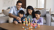 © fizkes - Indian couple playing construction blocks set together with little children. Siblings sit on floor at table, enjoy carefree playtime with parents. Loving family weekend leisure at home, creative games