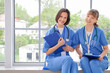 © Pixel-Shot - Female medical interns with clipboards sitting on windowsill in clinic