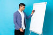 © luismolinero - Young Colombian man isolated on blue background giving a presentation on white board