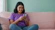 © Asad - woman is using a phone sitting on a pink sofa and green wall