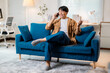 © Parichat - Happy young man using smartphone while relaxing on comfortable sofa at home