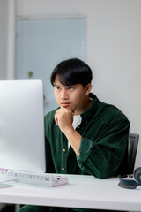 Young asian man working from his desk in a modern office, thinking about his next move in the project