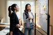 © Parichat - Two businesswomen are discussing and brainstorming using sticky notes on whiteboard in modern office