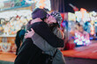 © qunica.com - Two friends embrace at a festive outdoor event, surrounded by vibrant lights and joy.