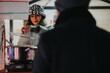 © qunica.com - A woman in winter clothing serves hot food from a stall to a customer on a chilly evening.