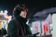 © qunica.com - A cheerful young man wearing warm clothes enjoying the atmosphere of a winter market. Festive lights and colorful decorations create a cozy and lively ambiance, highlighting the joy of the season.